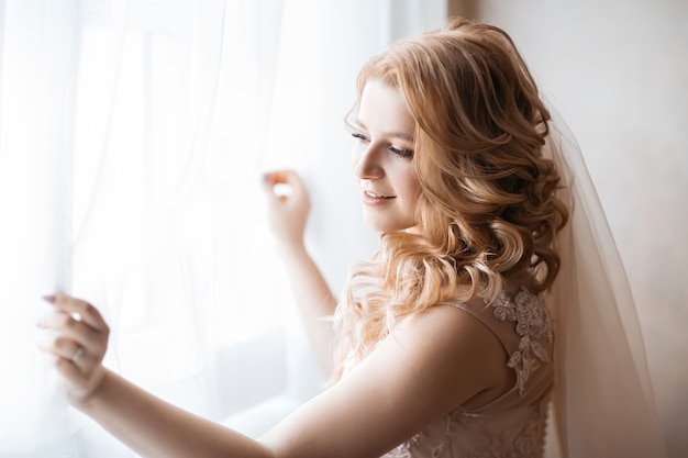 Photo fermer. jeune femme en robe de mariée debout près de la fenêtre. jours fériés et événements