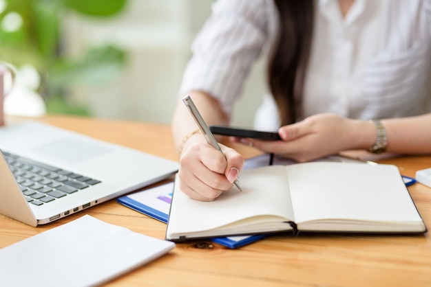 Fermer. Main de femme d'affaires utilisant un stylo prenant des notes et utilisant un smartphone au bureau.