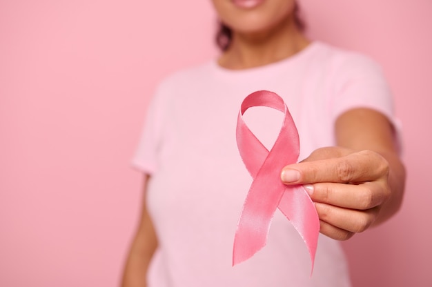 Fermer. Main de femme en t-shirt rose, tenant un ruban rose. Journée mondiale contre le cancer. Sensibilisation au cancer du sein et de l'abdomen, journée rose d'octobre sur fond coloré, espace de copie. Concept de soutien au cancer du sein