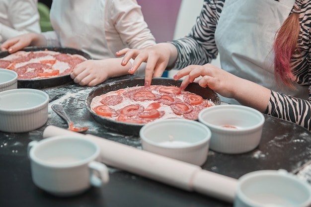 Fermer. une petite fille dispose des morceaux de tomates sur la base d'une pizza. cuisiner des pizzas ensemble