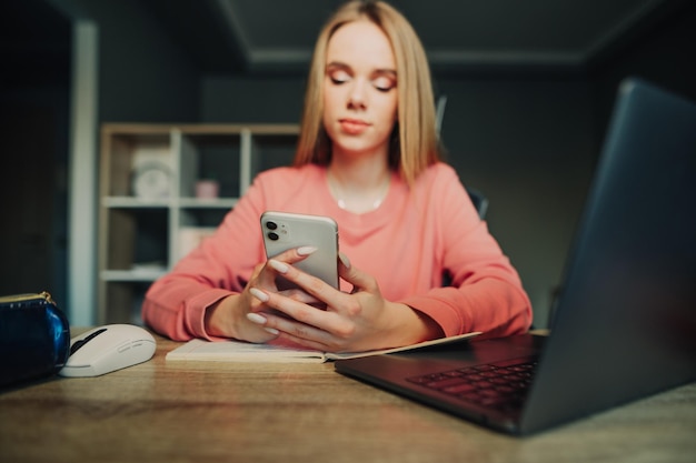 Fermer la photo Dame utilise le téléphone Étudiante assise au bureau à la maison avec un ordinateur portable