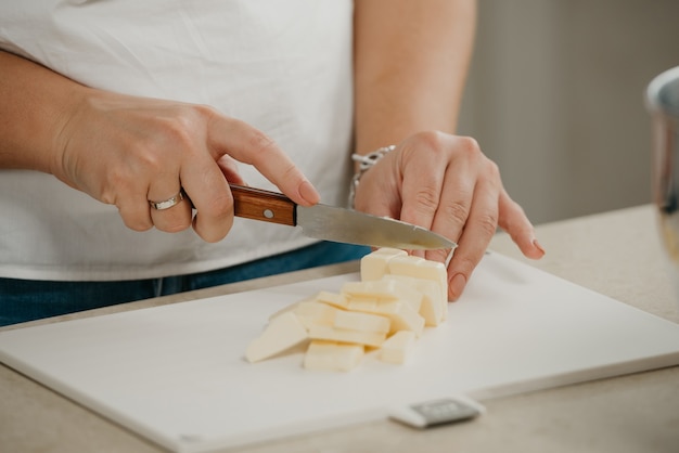 Fermer la photo des mains d'une jeune femme coupant du beurre de ferme frais sur une planche à découper avec un couteau bien aiguisé