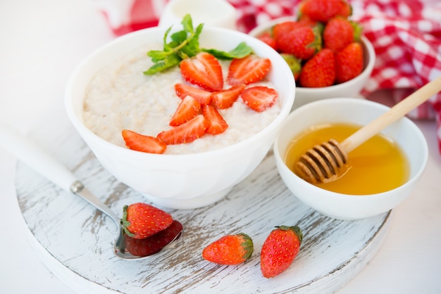 Fermer uo sain petit déjeuner équilibré de flocons d'avoine avec des fraises et du miel sur un mur blanc. Photo horizontale avec espace de copie.