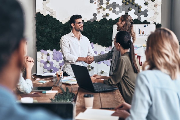 Fermez l'affaire. Jeunes hommes modernes en tenue décontractée intelligente se serrant la main et souriant tout en travaillant dans le bureau de création