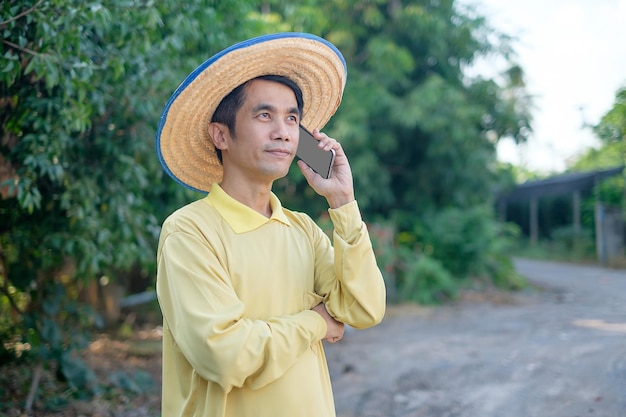 Un fermier asiatique porte une chemise jaune à l'aide d'un smartphone à la ferme