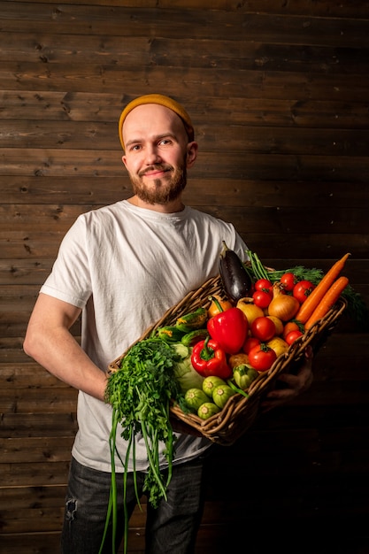 Un fermier heureux dans un tshirt blanc et un chapeau tient un panier de fruits et légumes frais