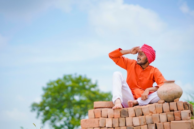 Fermier indien assis sur des briques et regardant le ciel