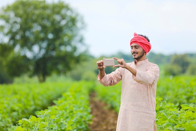 Fermier indien utilisant un smartphone sur le terrain agricole.