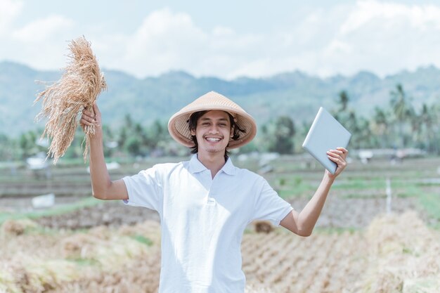 Le Fermier Portant Un Chapeau Lève La Main Lorsqu'il Transporte Des Plants De Riz Et Une Tablette Après La Récolte