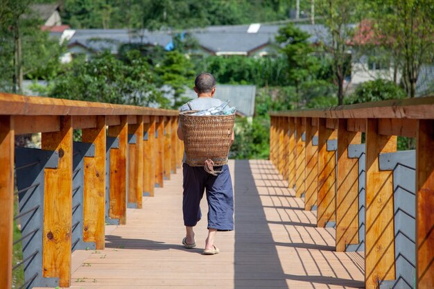 Fermier portant un panier sur son sac marchant sur un pont de bois au sommet de la rivière au Sichuan