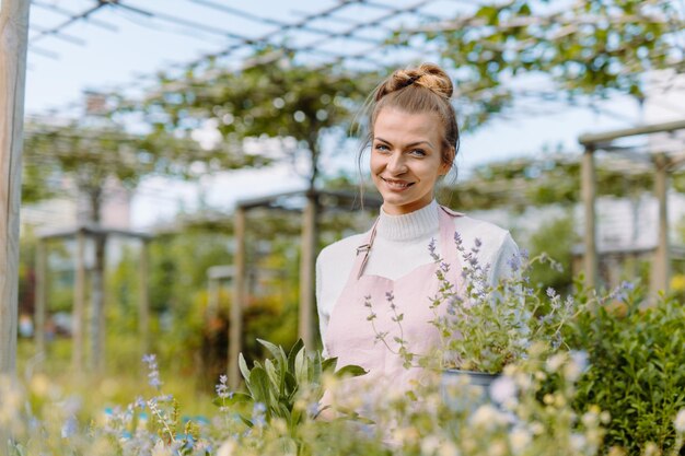 Fermière avec un pot de plantes fraîches debout à sa serre et regardant la caméra avec un sourire