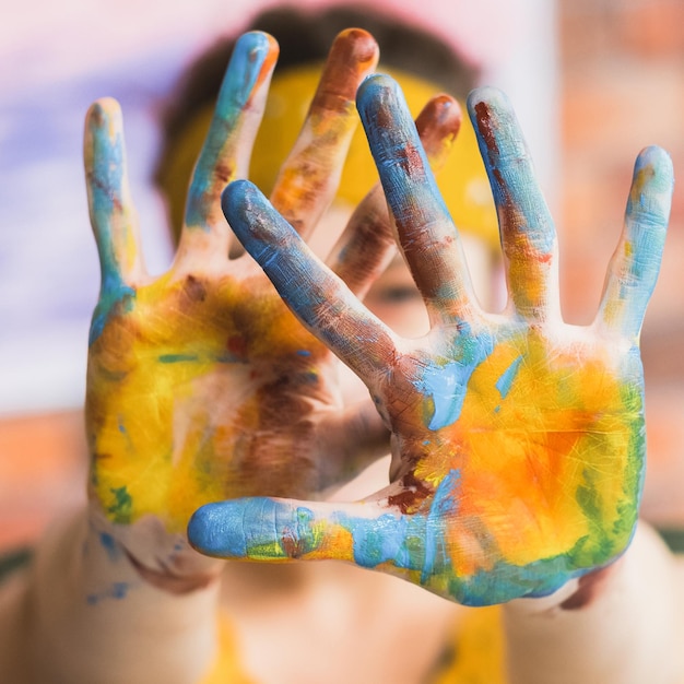 Festival d'art Femme peintre se cachant le visage derrière les mains ouvertes sales avec de la peinture colorée Arrière-plan flou