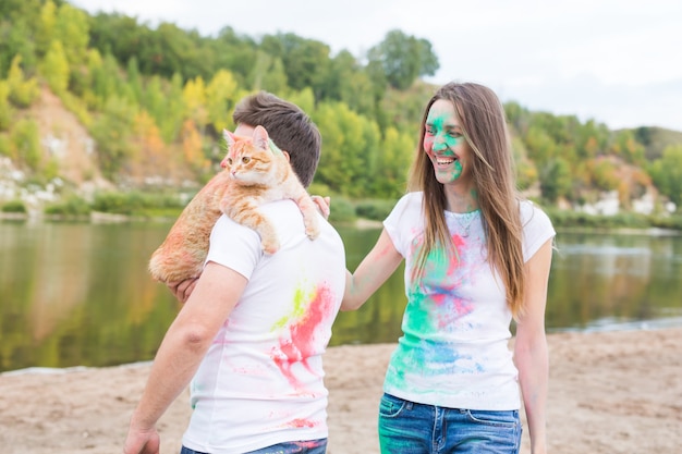 Festival holi, concept de tourisme et de nature - Portrait de femme et d'homme avec un chat couvert de poussière multicolore.