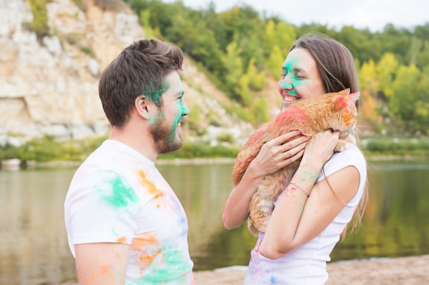 Festival holi, vacances, tourisme, animal de compagnie et concept nature - Portrait de femme et d'homme avec un chat couvert de poussière multicolore.