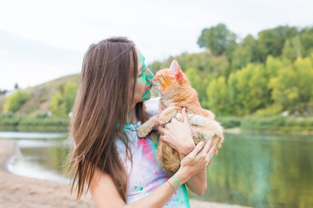 Festival holi, vacances, tourisme, animaux et nature concept - Portrait de femme avec chat couvert de poussière multicolore.