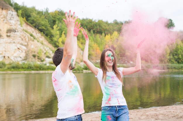 Festival holi, vacances, tourisme et concept nature - Couple vêtu de chemises blanches jouant avec la poussière colorée.