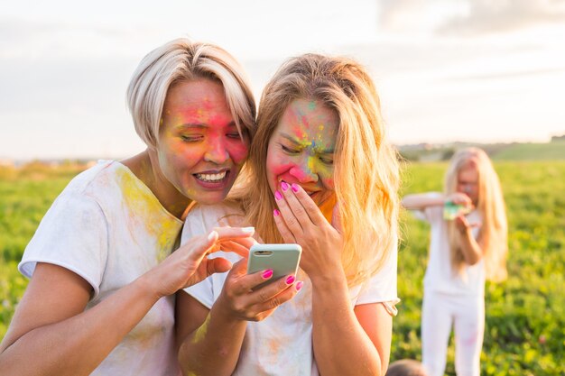 Festival indien de holi, concept de personnes - Deux filles qui rient avec de la poudre colorée sur les visages regardent