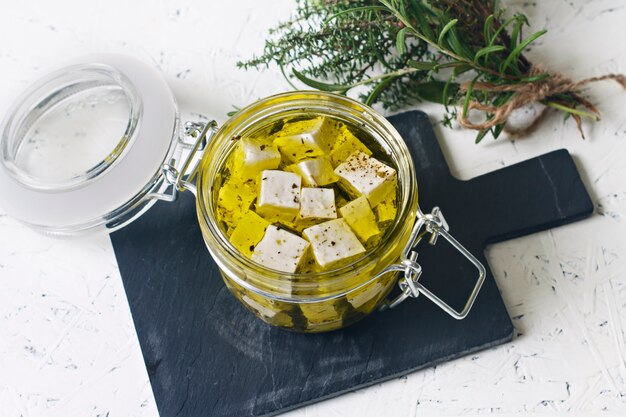 Feta marinée dans un bocal en verre et épices sur fond blanc