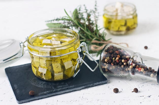 Feta marinée dans un bocal en verre et épices sur fond blanc