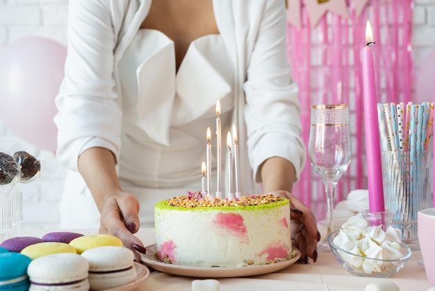 Fête d'anniversaire Tables d'anniversaire Jolie femme en vêtements de fête blancs préparant une table d'anniversaire avec des gâteaux macarons cakepops et autres sucreries