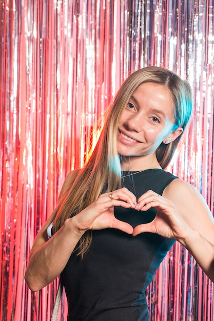 Fête d'anniversaire, vacances et concept glamour - femme souriante en robe de soirée fait un geste en forme de coeur sur fond de lumières