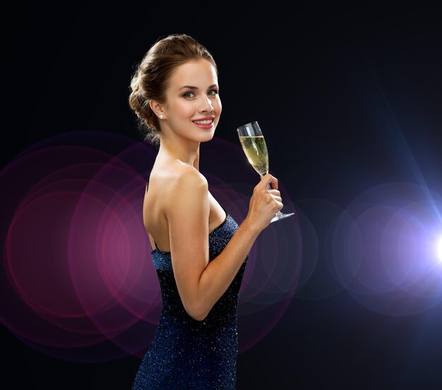 fête, boissons, vacances, personnes et concept de célébration - femme souriante en robe de soirée avec un verre de vin mousseux sur fond de lumières nocturnes