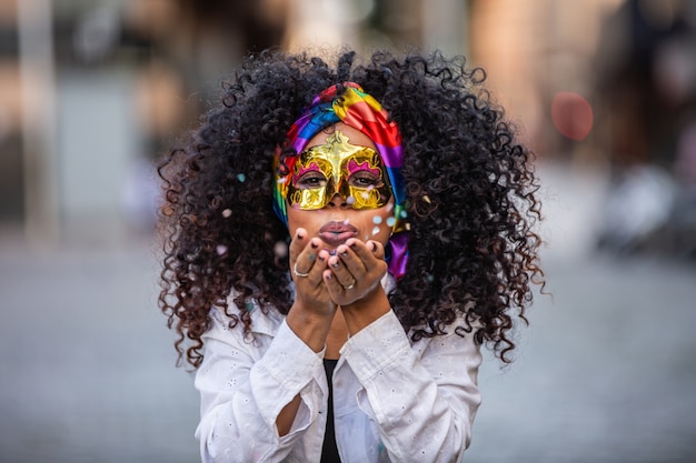 Fête du Carnaval. Brésilienne cheveux bouclés femme en costume soufflant des confettis