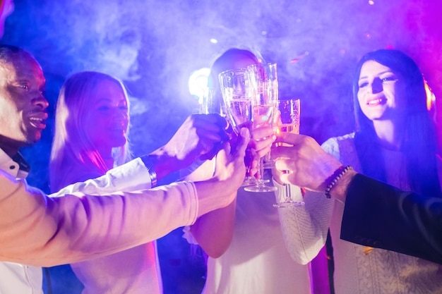 Fête du nouvel an, vacances, vie nocturne et concept de personnes - des amis souriants trinquent des verres de champagne en boîte de nuit