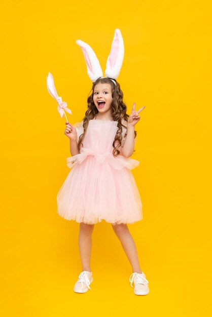 Fête des enfants de Pâques Une adolescente vêtue d'une robe luxuriante se réjouit au printemps L'enfant porte de longues oreilles de lapin Une belle petite fille aux cheveux longs sur fond jaune isolé