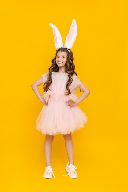 Fête des enfants de Pâques Une adolescente vêtue d'une robe luxuriante se réjouit au printemps L'enfant porte de longues oreilles de lapin Une belle petite fille aux cheveux longs sur fond jaune isolé