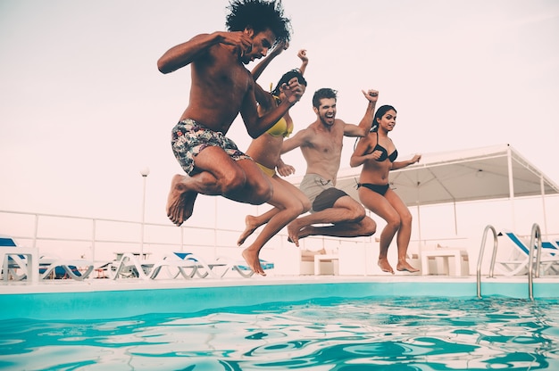 Fête d'été à la piscine. Groupe de beaux jeunes qui ont l'air heureux en sautant ensemble dans la piscine