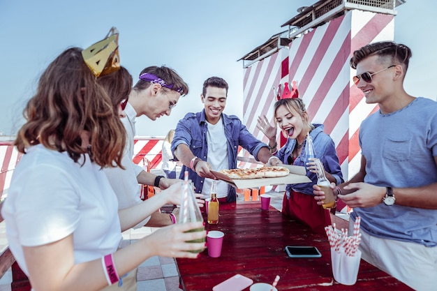 Fête de la gastronomie. Fille heureuse levant la main tout en allant manger de la pizza avec de la bière