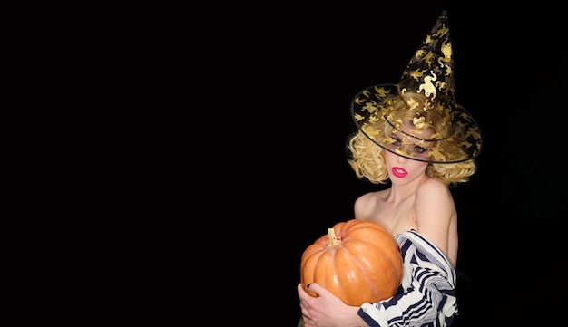 Fête d'Halloween fille sensuelle en chapeau de sorcière avec citrouille sorcière femme sexy avec les épaules nues tient