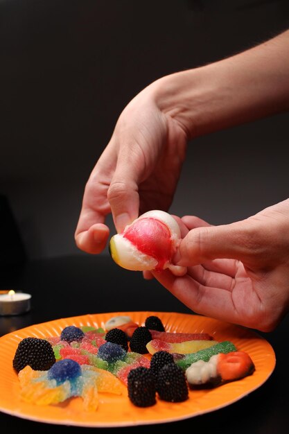 Photo fête d'halloween les mains brisent un œil de gelée blanc et jaune libérant un liquide rouge bonbons et sucreries