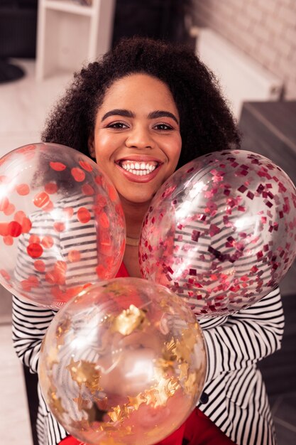 À la fête. Heureuse femme positive souriant tout en tenant de beaux ballons