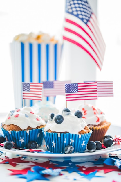 fête de l'indépendance, célébration, patriotisme et concept de vacances - gros plan de cupcakes ou de muffins glacés décorés de drapeaux américains et de myrtilles sur une assiette à la fête du 4 juillet