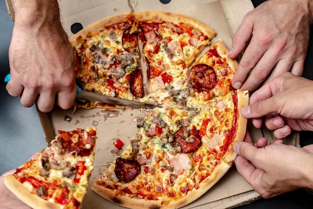 Fête à la maison La main de l'homme coupe la pizza et des amis heureux cassent un morceau