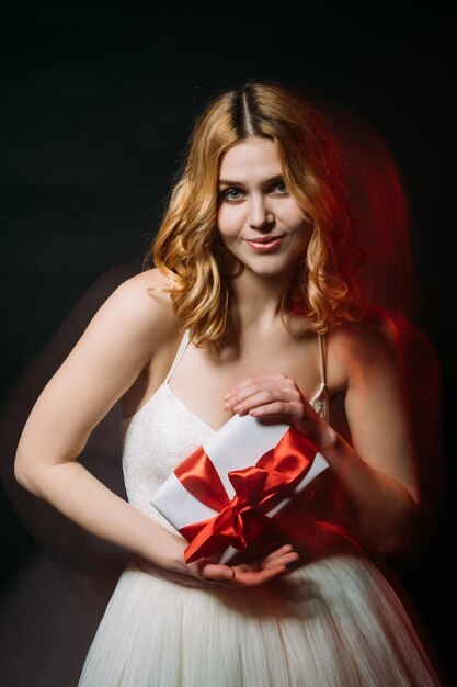 Fête de mariage femme heureuse cadeau de vacances salutation festive jolie femme souriante tenant une boîte-cadeau ruban rouge longue exposition flou lumière rouge noir isolé