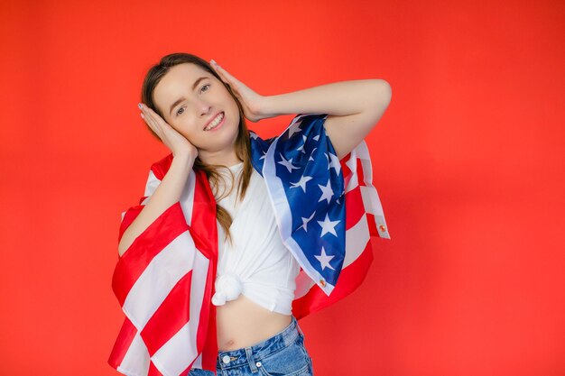 Fête patriotique Heureuse jeune femme avec drapeau américain sur fond rouge Les États-Unis célèbrent le 4 juillet