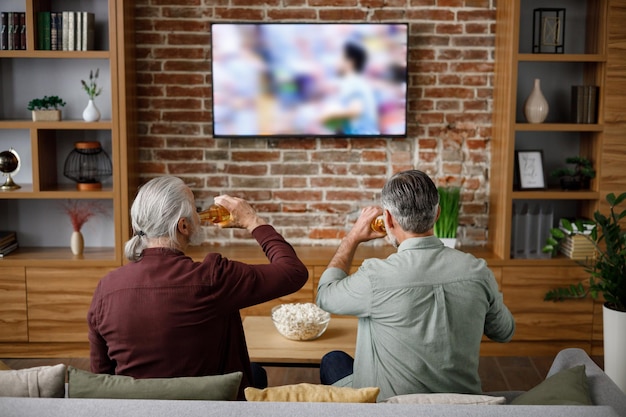 Fête des pères Fils adulte avec un père âgé regardant un match de football à la télévision et célébrant la victoire assis sur un canapé à la maison Une famille de deux générations aime passer du temps ensemble Sport et divertissement