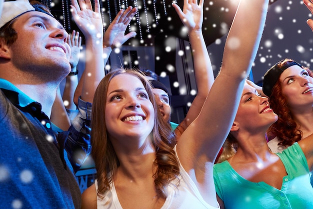 Photo fête, vacances, célébration, vie nocturne et concept de personnes - amis souriants agitant la main au concert en club et effet de neige