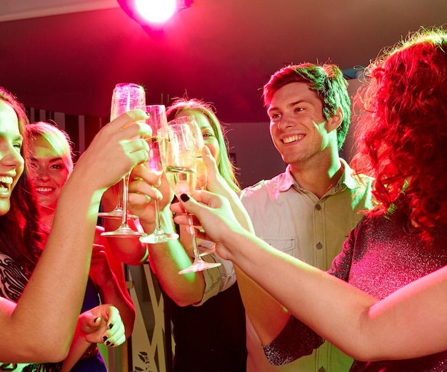 fête, vacances, fête, vie nocturne et concept de personnes - amis souriants qui trinquent dans des verres de champagne en club