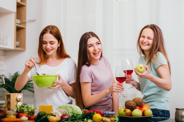 Fête végétalienne féminine. Jeunes femmes en t-shirts s'amusant. Assortiment de fruits et légumes. Alcool de vin rouge.