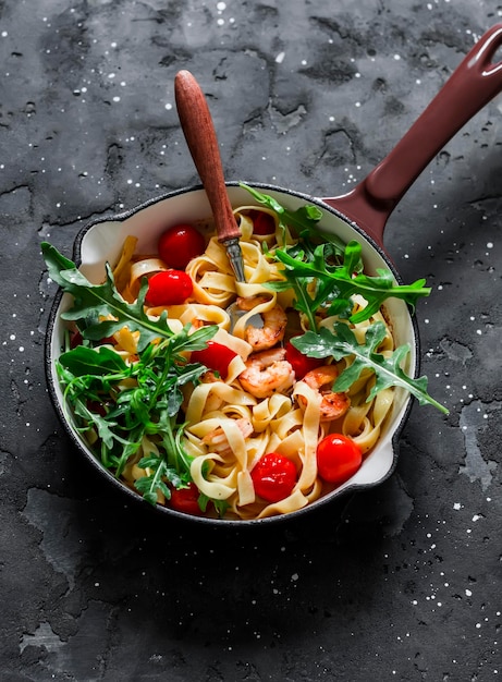 Fettuccine aux crevettes tomates cerises et roquette dans une poêle à frire sur fond sombre Vue de dessus Délicieux déjeuner à l'italienne