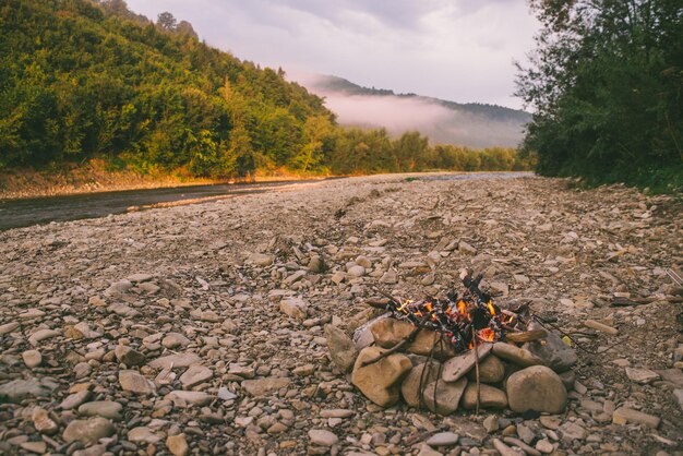 Feu de camp au lever du soleil au bord de la rivière des rochers dans les montagnes