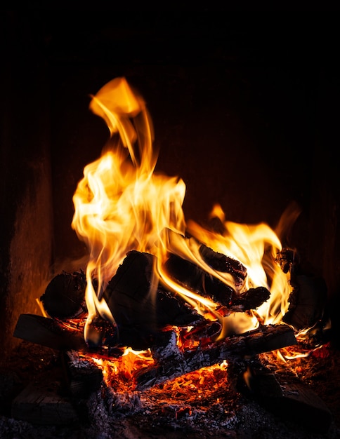 Feu dans la cheminée. Flammes et bois de chauffage carbonisé sur fond sombre