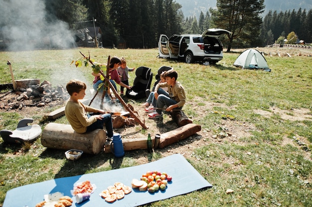 Feu de joie familial en montagne. Faire frire des saucisses. Mère avec quatre enfants en camping. Randonnée d'automne et météo du camp. Réchauffement et cuisson près de la flamme ensemble.