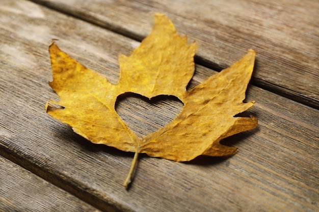 Feuille d'automne séchée avec coeur découpé sur fond en bois