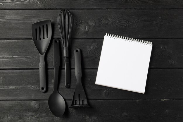 Feuille blanche de bloc-notes ouvert et d&#39;ustensiles de cuisine sur la table avec une nappe, espace de copie