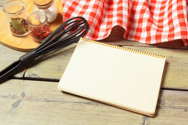 Feuille blanche de bloc-notes ouvert et d&#39;ustensiles de cuisine sur la table avec une nappe, espace de copie